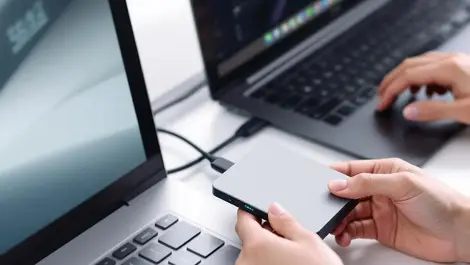 Realistic compact external hard drive connected to modern desktop hands handling